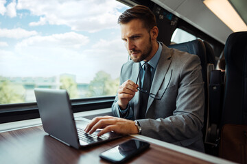 Handsome middle age businessman using his laptop computer while traveling with high-speed train. Modern and fast travel concept.