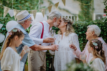 Mature bride and groom kissing at wedding reception with their family, outside in the backyard.