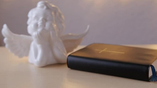 old black book, family bible in dark cover, white ceramic figurine of angel with wings, goose feather, concept of intermediary between God and world, eternal Christian values, unity of people in faith