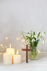 Wooden cross, snowdrops flowers and candles on table, blurred abstract background. Religious church holiday. symbol of faith in God, Christianity Feast, Easter, Palm Sunday, Lent