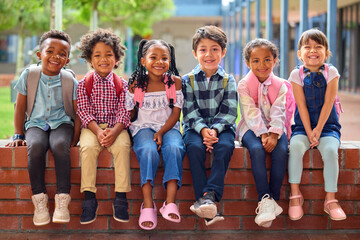 Portrait Of Multi-Cultural Elementary School Pupils Sitting On Wall Outdoors At School