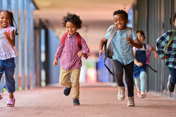 Obraz premium Group Of Multi-Cultural Elementary School Pupils Running Along Walkway Outdoors At School
