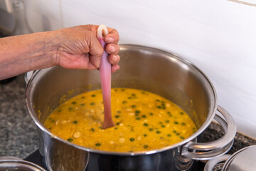 hand of a grandmother mixing the ingredients of the fanesca that is being cooked in a pot