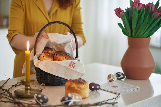 Woman with candle, preparing Easter basket with embroidered towel at kitchen home with tulips standing on the table. High quality photo