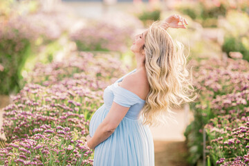 Fototapeta na wymiar Barriga da mamãe grávida com vestido azul, a espera do bebê, entre as flores no campo. Cabelo loiro ao vento