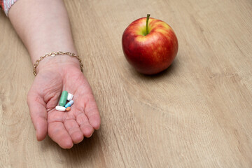 A woman's hand with medicines next to an apple lying on the table