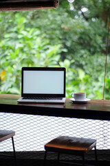 laptop with white screen and a coffee in white cup on the table garden view