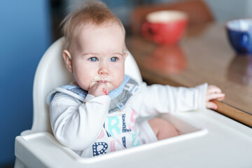 Funny portrait of a baby toddler with a dirty face sitting in the kitchen in a high chair