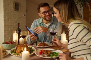 Happy couple enjoying food and wine while surfing the net