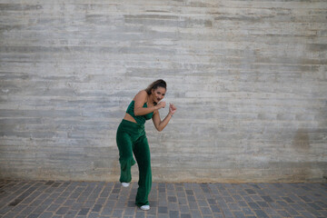 Latin woman, young and beautiful dancing modern dance on gray cement background. Woman kicks in the air. Modern dance and dance concept.