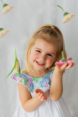Cute little girl 3 years old with blond hair with colored flowers on white background. Spring. Holidays. Happy child.