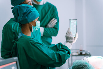 Surgery team and nurse looking on vr x-ray scan result on digital tablet in operating room at...