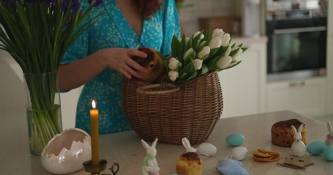 Woman smiling, preparing Easter basket with white tulips at kitchen home. High quality photo