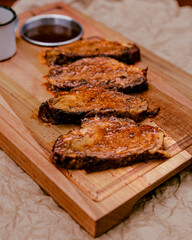 roasted smoked brisket on top of a wooden board and barbecue sauce on the side