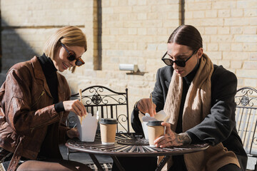 stylish couple eating asian food from carton boxes near paper cups on metallic bistro table.