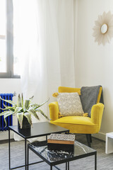 Corner of an apartment decorated with a yellow armchair with black metal coffee tables and one with a polished black marble top