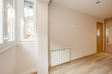 Empty room of a house with aluminum windows, radiator of the same material and oak carpentry on doors and floors