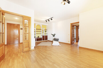 Living room of an empty house with double wooden access doors, a built-in bookcase with plaster...
