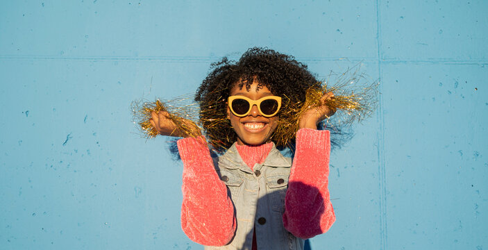 Happy woman holding golden tinsel in front of blue wall