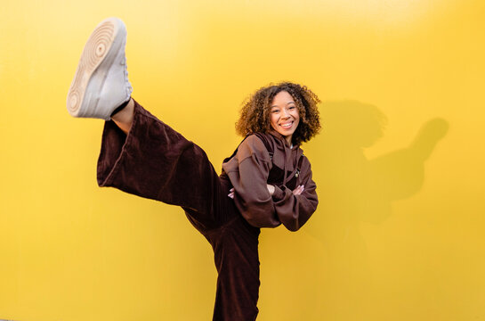 Smiling woman with arms crossed kicking in front of wall