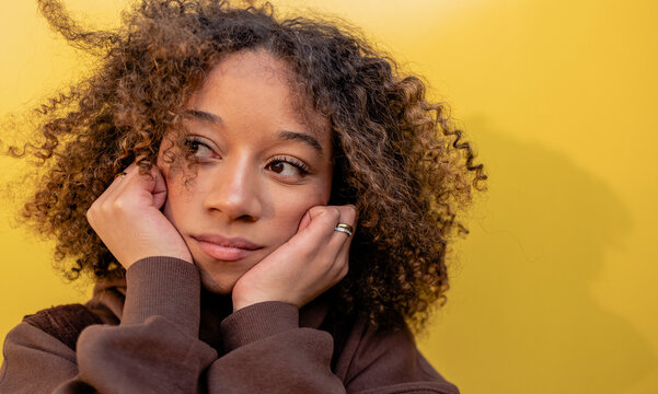 Thoughtful woman with curly hair in front of wall
