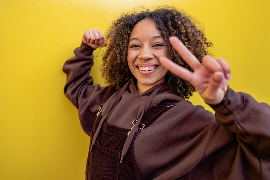 Smiling woman with curly hair gesturing peace sign