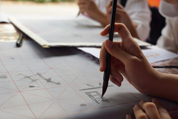Asian students practice the art of Chinese calligraphy by writing Chinese characters, the word...