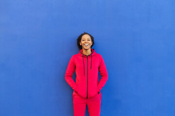Happy woman with hands in pockets leaning on blue wall