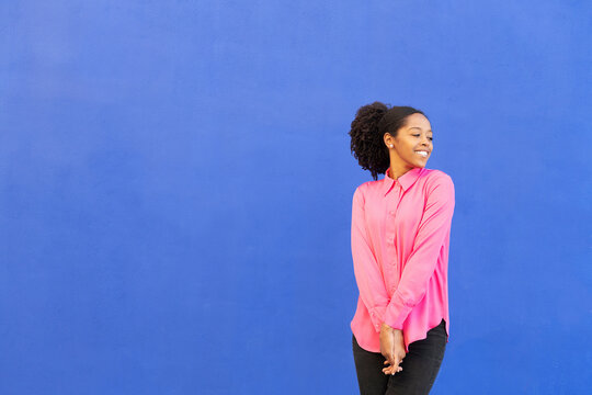 Happy woman wearing pink shirt in front of blue wall