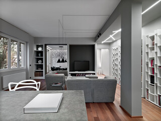 Interior view of a modern living room with a wooden floor and bookcase in the background there is the dining room