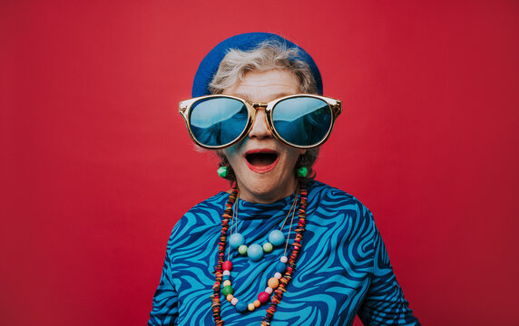 Surprised senior woman wearing big sunglasses against red background