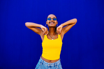 Happy young woman wearing sunglasses in front of blue wall