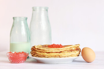 A stack of thin pancakes with caviar on a light background. Glass bottle with milk, crepes, caviar and egg. A week of pancakes. Maslenitsa