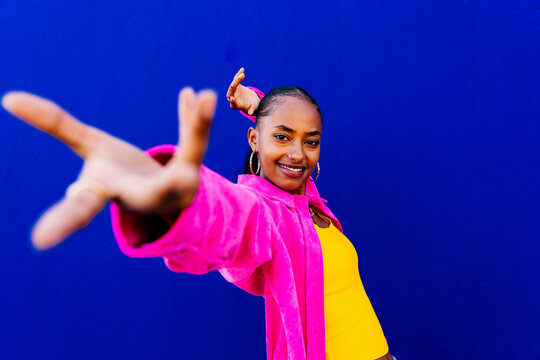 Smiling young woman dancing in front of blue wall
