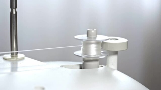 The process of winding thread on the bobbin of a modern sewing machine. Close-up of a spool with white thread. Professional sewing equipment detail, working tool