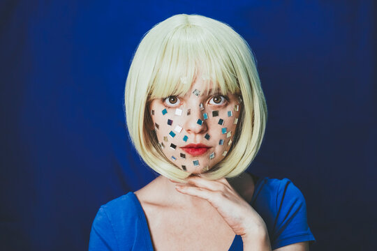 Blond woman with small mirrors on face against blue background