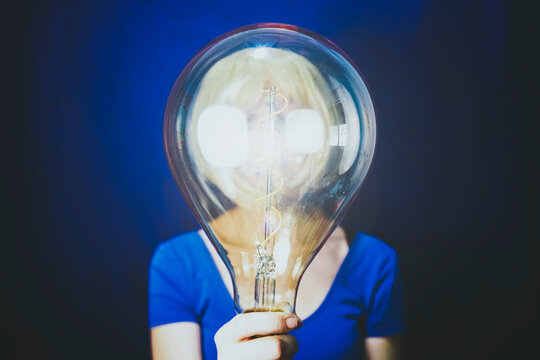 Woman holding large illuminated bulb against blue background