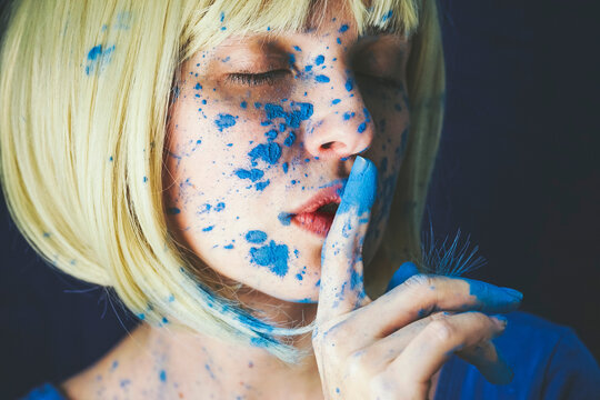 Woman with blue powder paint and finger on lips against black background