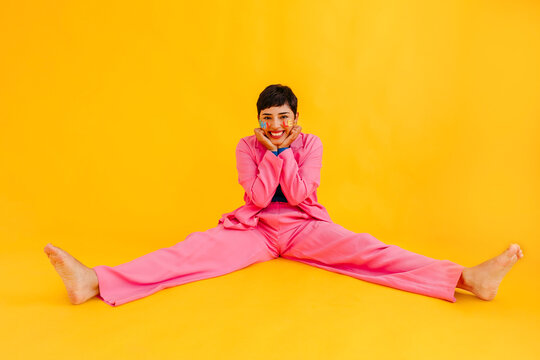 Happy young woman sitting with legs apart in over yellow background