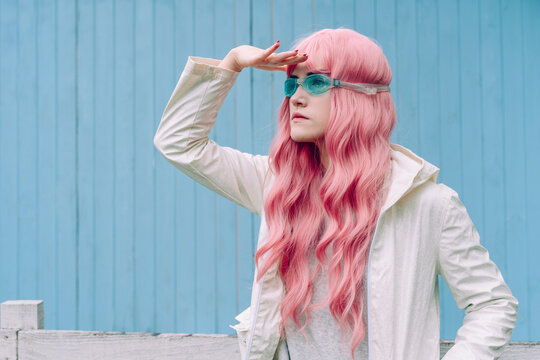 Young woman with pink hair searching in front of blue wall
