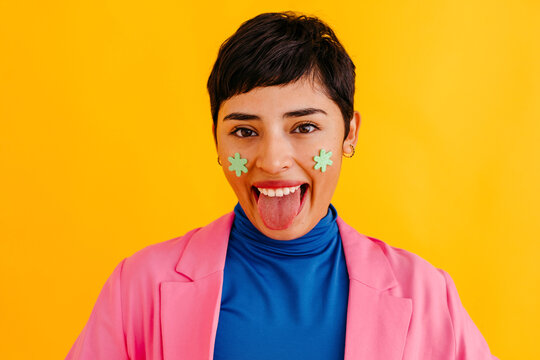 Young woman sticking out tongue against yellow background