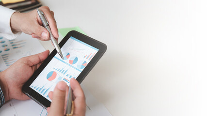 Two businessman analyzing and discussing graph, charts and diagrams while one of them pointing at tablet screen at meeting. Business, graphs and charts on the screen of a digital tablet.