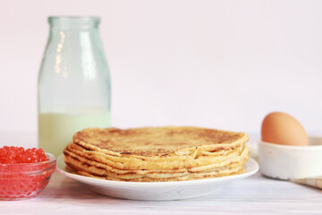 A stack of thin pancakes with caviar on a light background. Glass bottle with milk, crepes, caviar and egg.