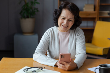 European middle aged senior woman holding using smartphone touch screen typing scroll page. Stylish older mature 60s lady with cell phone using internet social media apps at home. Shopping online