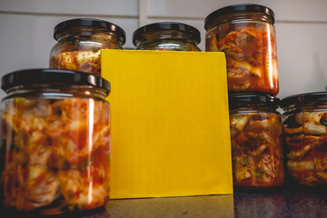 Spicy traditional kimchi in glass jars and yellow board with copy space in kitchen (kimchi: mix of pickled and fermented vegetables, garlic, chili peppers, salt)
