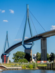 Portrait view of the tall blue dilapidated Köhlbrandbrücke suspension bridge seen from beneath from the riverside of harbor Rugenberger Hafen, landmark of the Port of Hamburg at a sunny summer day.