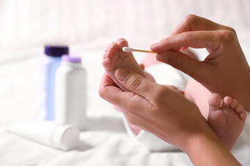 Mother cleaning baby's foot with cotton bud on bed, closeup