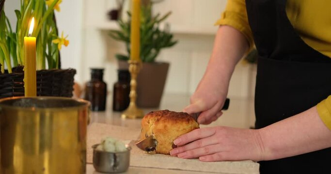 Woman cutting Easter cake, preparing Easter basket with embroidered towel at kitchen home with daffodils standing on the table. High quality photo
