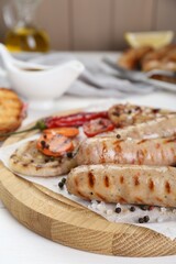 Tasty grilled sausages with vegetables and spices on white wooden table, closeup