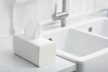 Package of paper towels on white countertop near sink in kitchen. Space for text